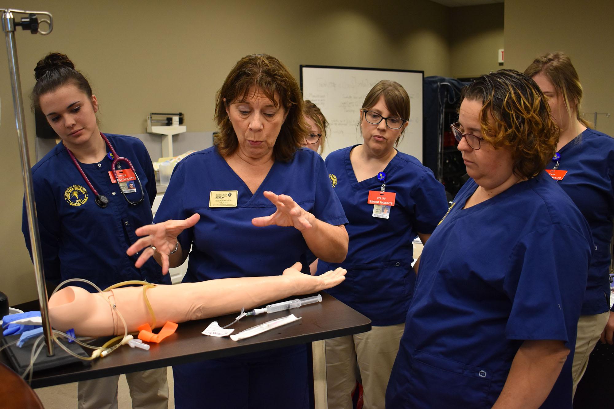 A nursing professor showing her class a fake arm for practicing inserting needles