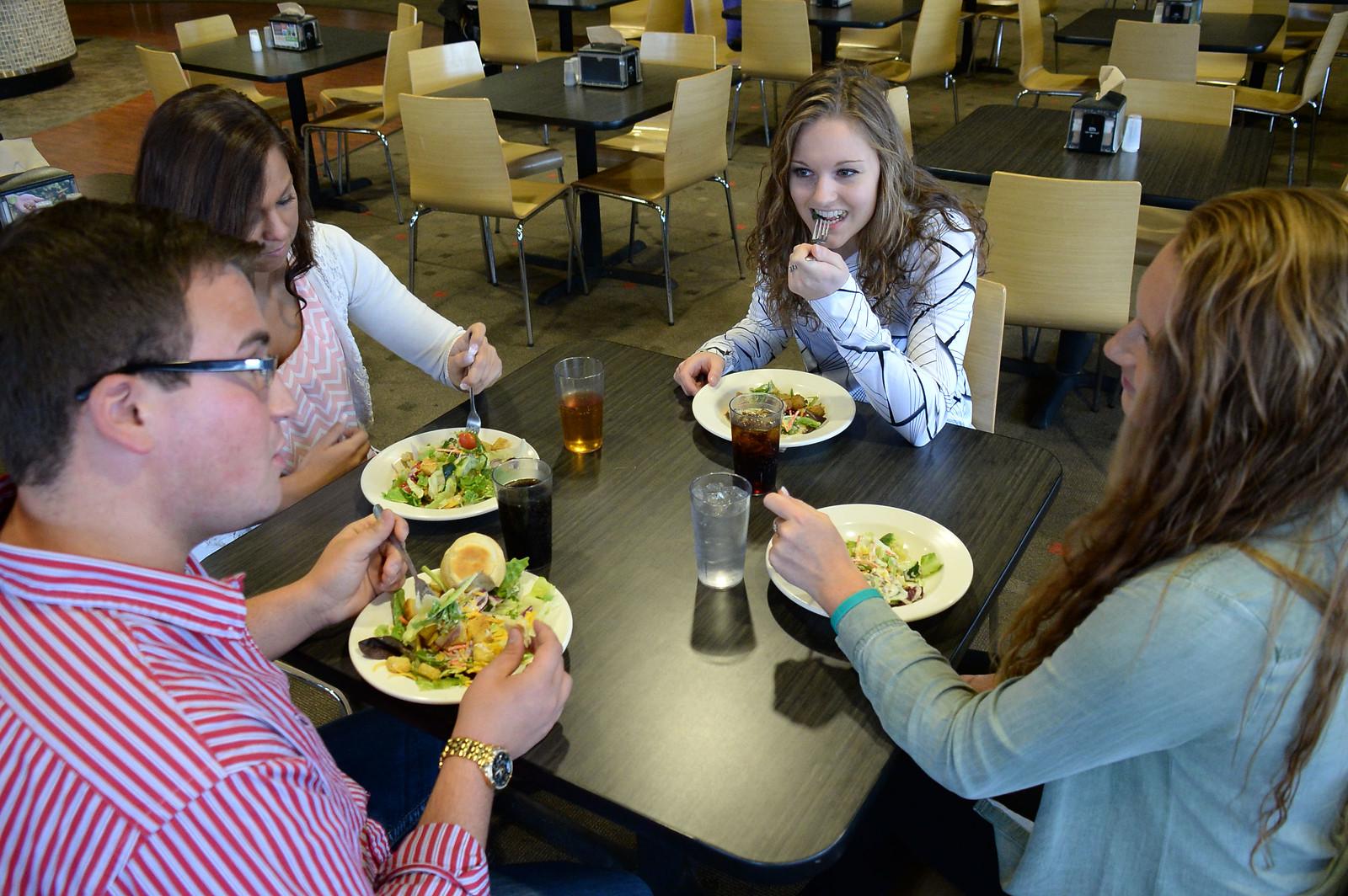 Four students sitting together at a table and eating salads
